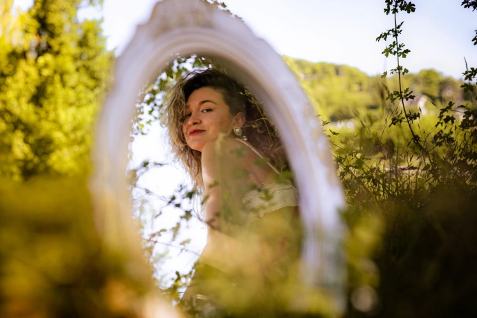 Au travers d'un miroir posé dans le champ à Gaillon, nous voyons la femme modèle nous sourire durant ce shooting photo portrait.