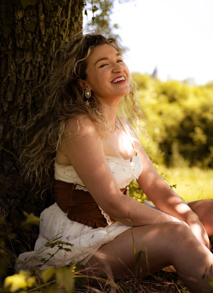 La femme prise en photo par le photographe à Gaillon est adossée contre un arbre, souriante à l'ombre. Derrière, le champ est ensoleillé.