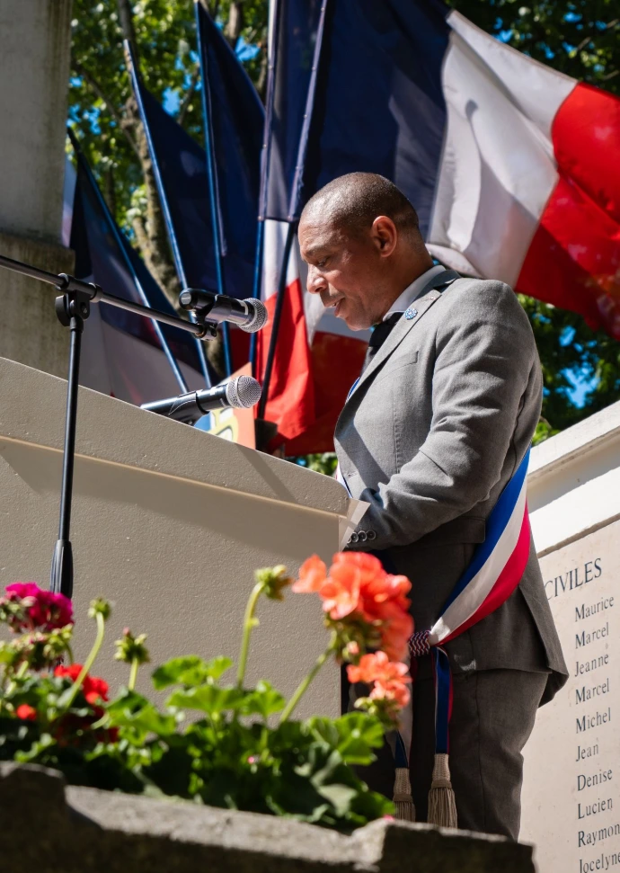 L'adjoint au Maire Karim Ternati debout devant un pupitre. Le drapeau français flotte derrière lui.