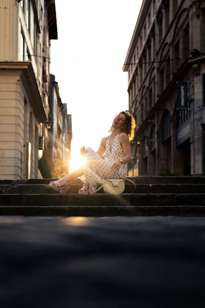 Une jeune femme, prise en photo pendant un shooting en contre plongée, assise sur des marches dans Rouen avec un soleil rayonnant derrière elle.
